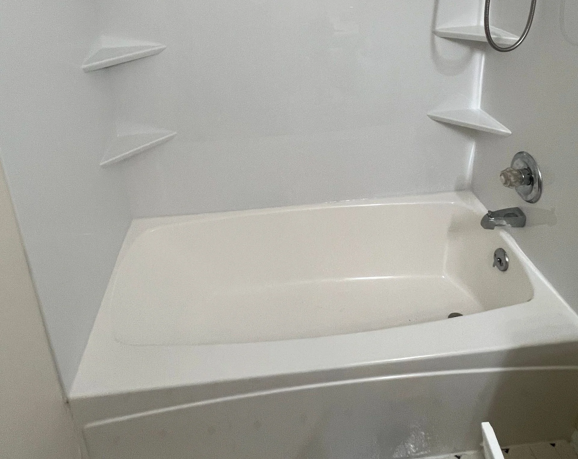 White bathtub in a small bathroom with a showerhead, faucet, and corner shelves above it