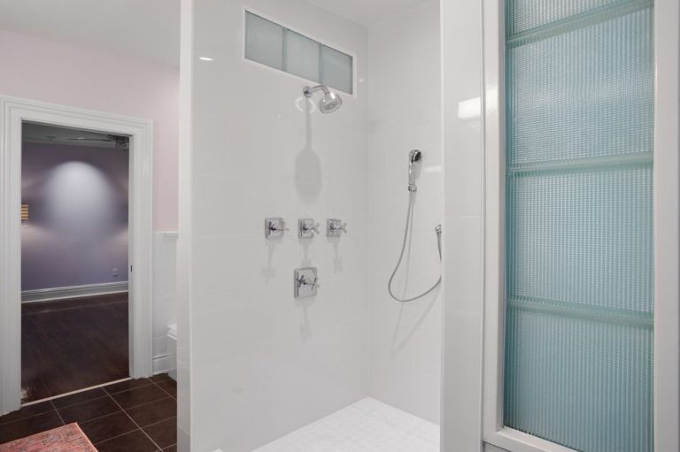 White bathroom shower with glass block window, silver fixtures, and a glass door.