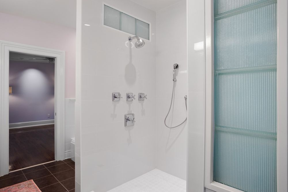 White bathroom shower with glass block window, silver fixtures, and a glass door.