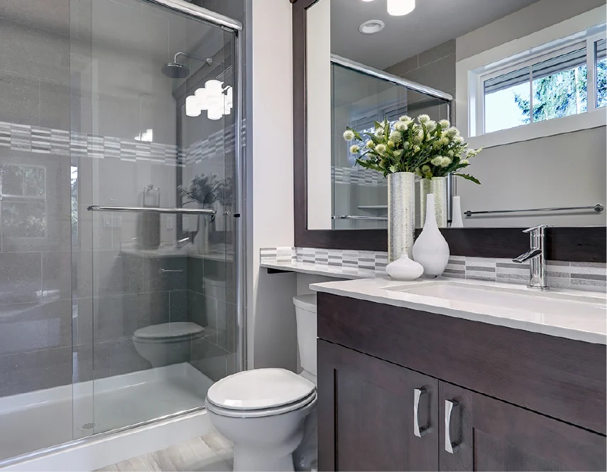 Modern bathroom with glass shower, toilet, dark vanity, white countertop, and vase of flowers