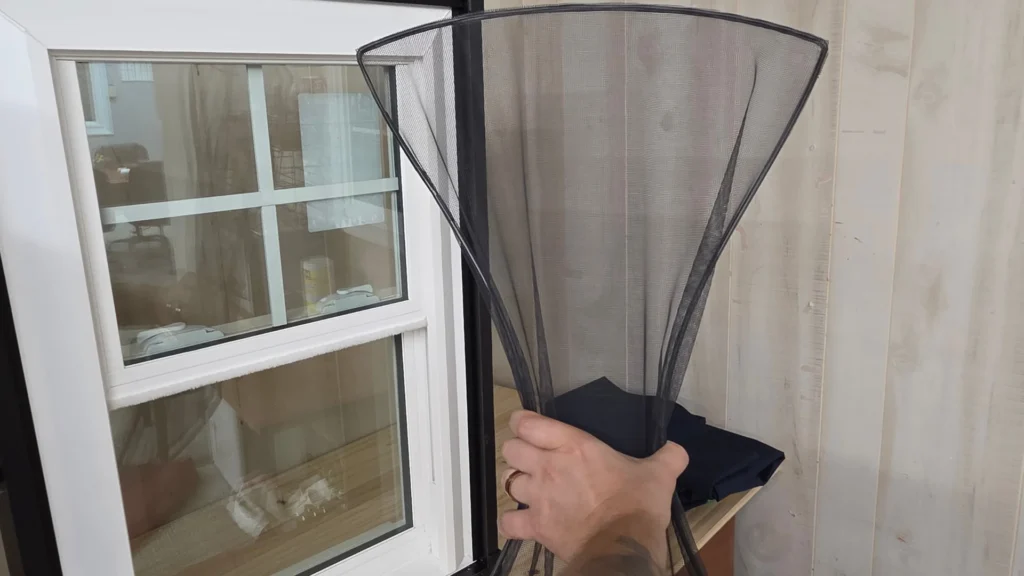 Hand holding a black FlexScreen near a window and light wood siding