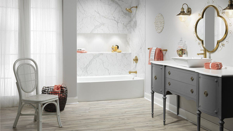 Bathroom with marble shower and vanity, gold fixtures, white walls, and a vintage chair.