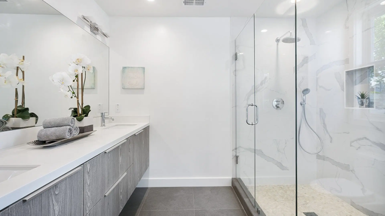 Modern bathroom with white walls, gray vanity, glass shower, and orchids.