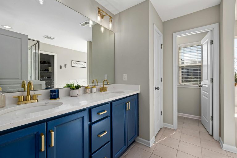 Bathroom with navy blue vanity, gold fixtures, and a white countertop. Doorway leads to a window.