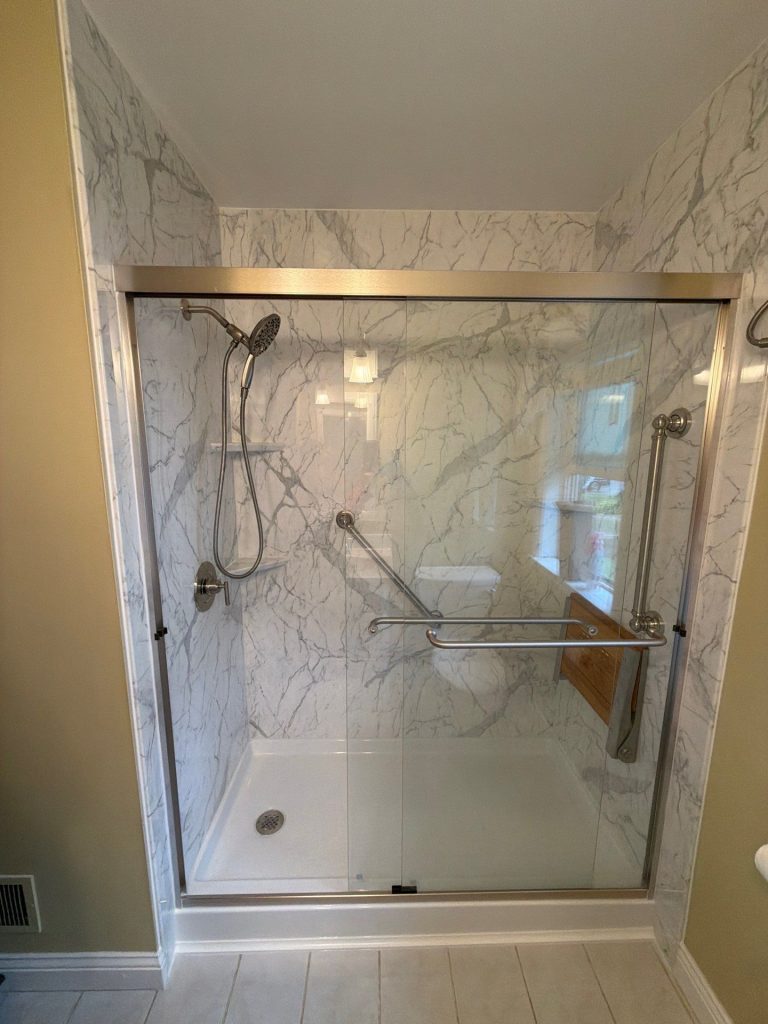 Modern glass walk-in shower with chrome fixtures, marble-look tile, and built-in corner bench.