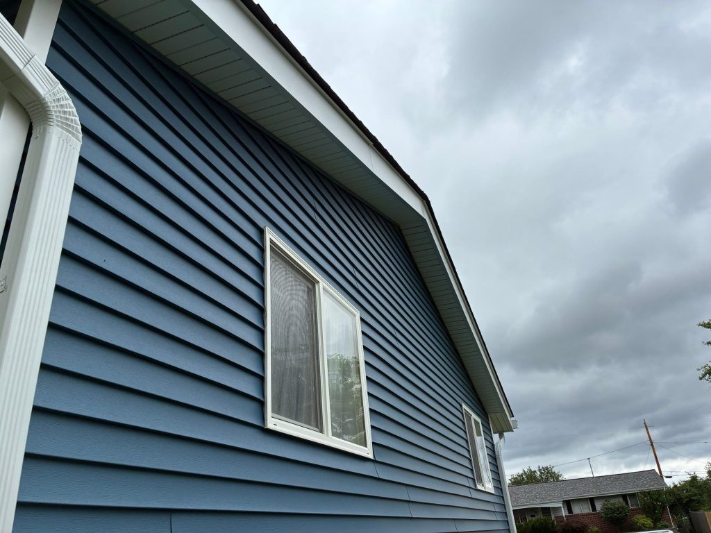 Side of a Florissant, MO home with blue vinyl siding, a white downspout and new white soffit and fascia.