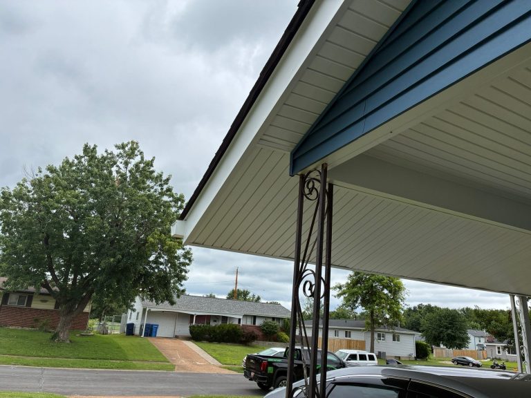 White soffit and fascia on a front porch overhang with blue siding above, looking out to the street in Florissant, MO.