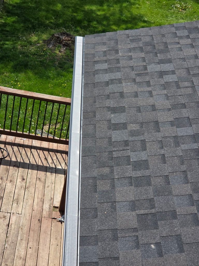 Gutter guard installed along the eave of a gray shingle roof above a wooden deck in St. Charles, MO.