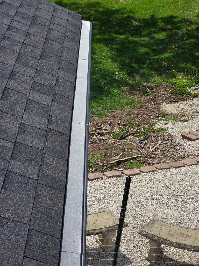 Finished gutter guard along a shingle roof edge above a gravel patio with stone benches in St. Charles, MO.