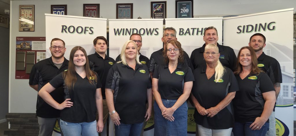 The Perfect Choice Home Solutions St. Louis management team in black company polos, standing in the St. Charles showroom in front of Roofs, Windows, Baths and Siding banners.