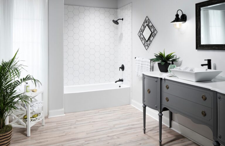 A white tub with a white hexagon tile-look wall surround and black fixtures, beside a gray vanity with a vessel sink.