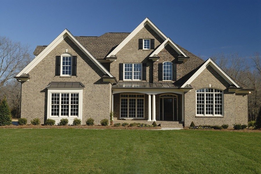 A two-story brick home with white grid windows, black shutters and a green front lawn.